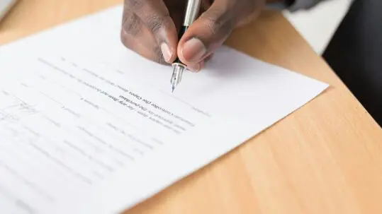 a hand holding a pen about to sign a paper