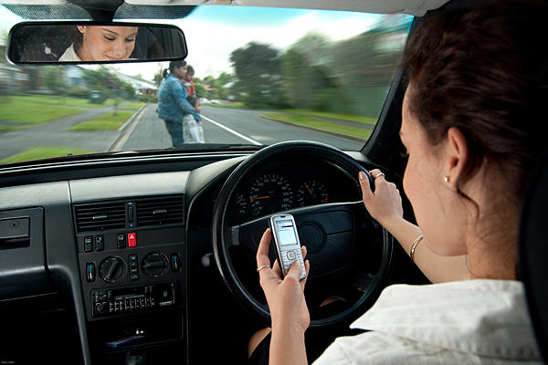 woman texting and driving as women with kids walk in front