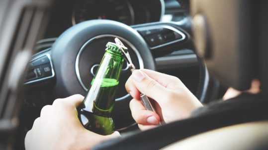 person opening beer bottle in driver's seat