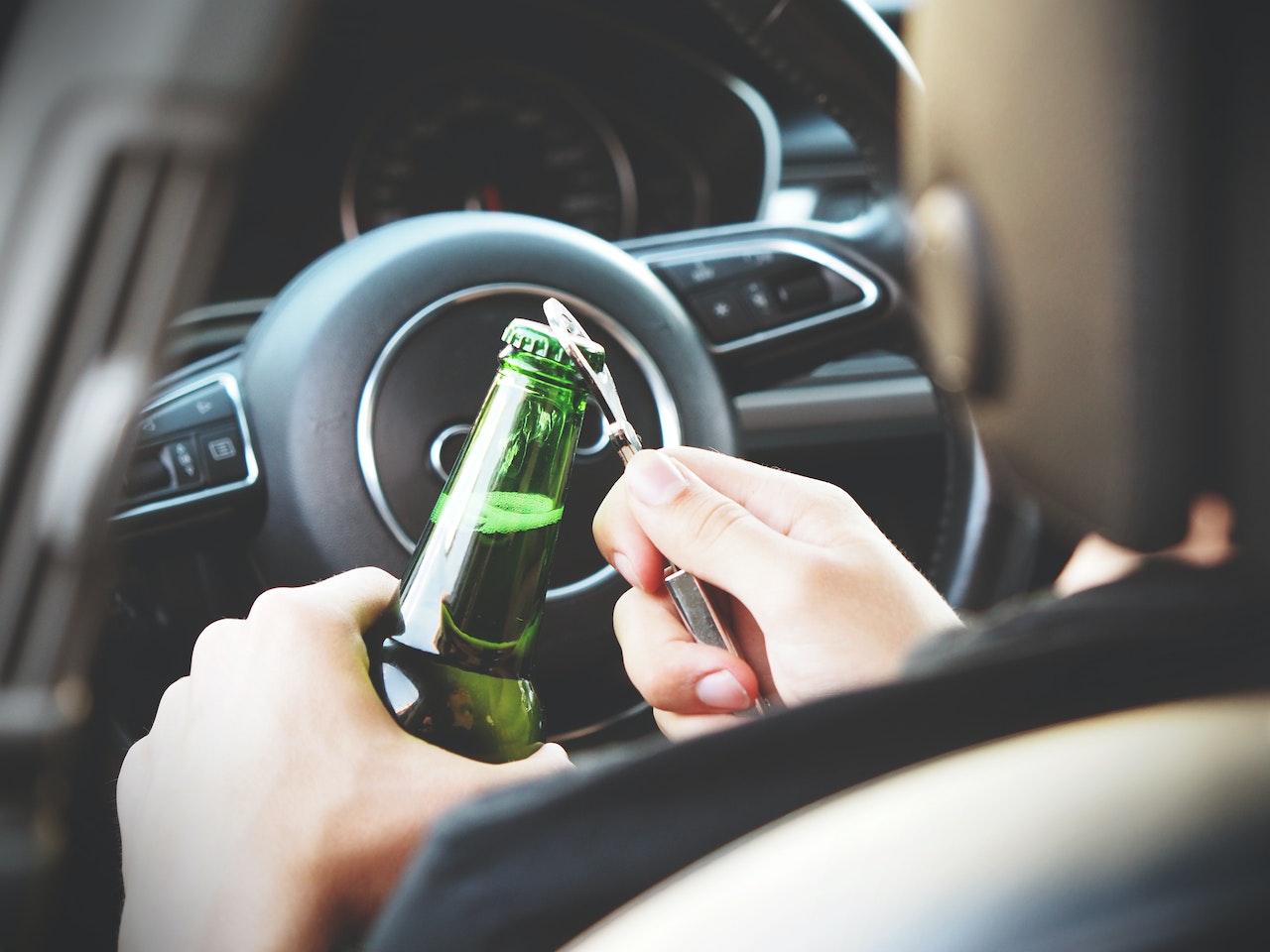 person opening beer bottle in driver's seat