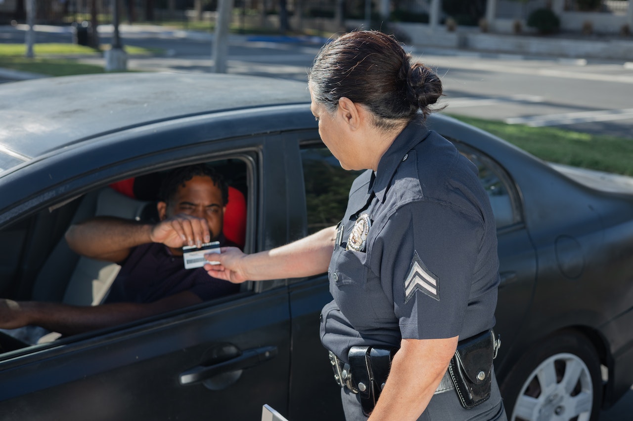 man in car handing license to female cop