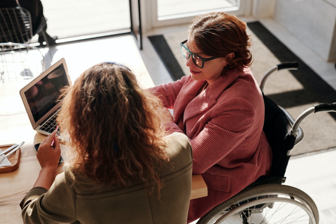 woman in wheelchair looking at computer with other woman